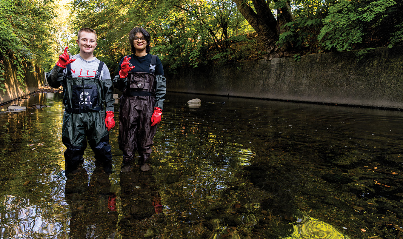 Two students, a man and a woman, stand in a river