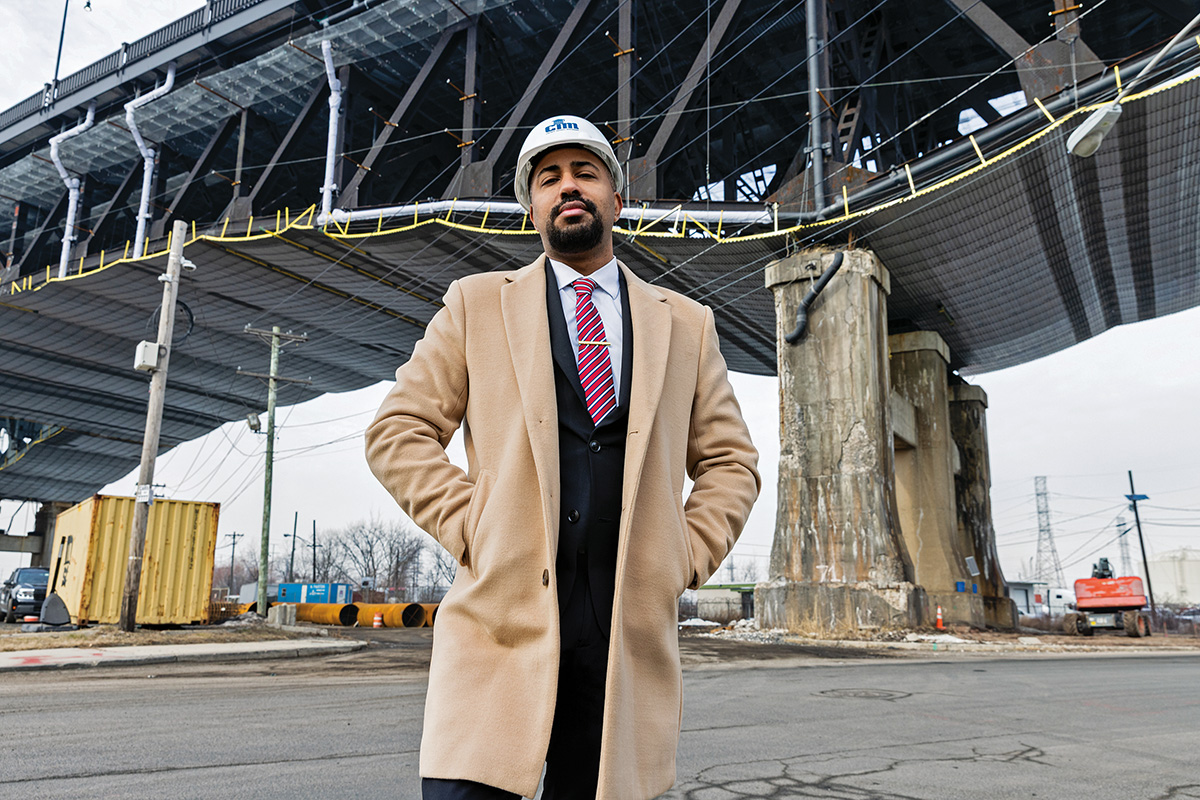 A man wearing a hard hat stands beneath a bridge