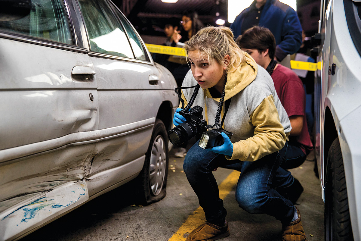 woman holding a camera near a car in a mock crime scene