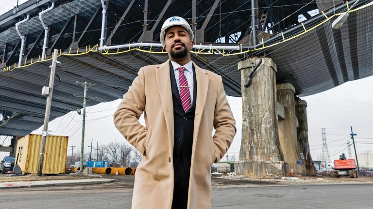 A man wearing a hardhat stands under a bridge